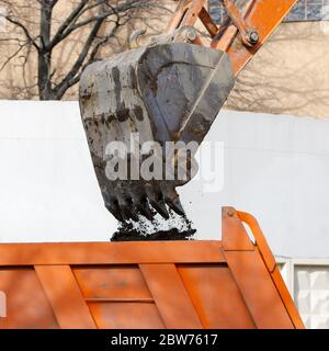 Das ausgeschnittene Bild des Baggers lädt den Boden in den Körper des roten Kipper, Nahaufnahme. Stockfoto