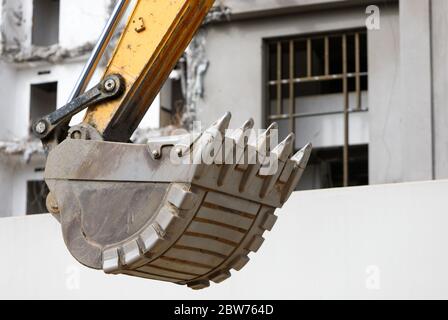Nahaufnahme des Baggers (Grader, Traktor) Eimer, zerstörtes Gebäude auf Hintergrund. Stockfoto