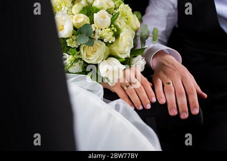 Hände von Braut und Bräutigam mit Ringen und Blumenstrauß Stockfoto