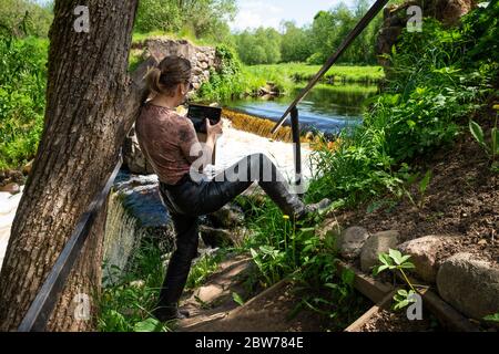 Eine Frau fotografiert mit einer Tafel einen künstlichen Wasserfall, die Reste einer hydraulischen Struktur auf dem Fluss Vyata, Miorski Bezirk, Weißrussland Stockfoto