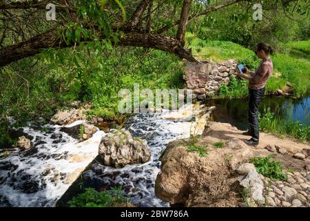 Eine Frau fotografiert mit einer Tafel einen künstlichen Wasserfall, die Reste einer hydraulischen Struktur auf dem Fluss Vyata, Miorski Bezirk, Weißrussland Stockfoto