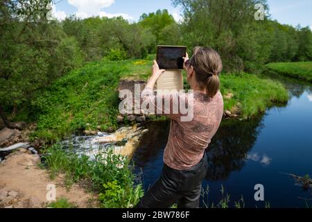 Eine Frau fotografiert mit einer Tafel einen künstlichen Wasserfall, die Reste einer hydraulischen Struktur auf dem Fluss Vyata, Miorski Bezirk, Weißrussland Stockfoto