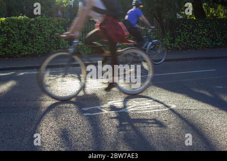Zwei Radfahrer passieren einander auf einer ruhigen Radroute, die durch die Fahrradschablone auf der Straße markiert ist. Es ist Abend und die Radfahrer werfen lange Schatten. Stockfoto