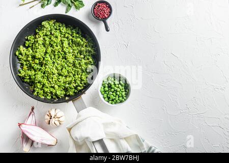 Mushy Erbsen Rezept gekochte Pfanne und Erbsen in Schüssel mit Minze Schalotte Pfeffer und Salz über weißen Stein Oberfläche Bio Keto Lebensmittel Draufsicht lat flay ov Stockfoto