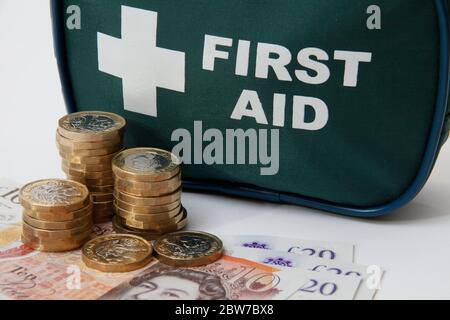 Britische Banknoten und 1£-Münzen vor einem erste-Hilfe-Beutel Stockfoto