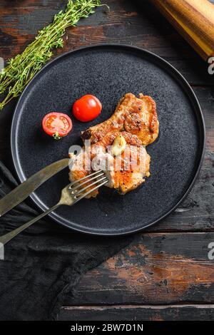 Gericht von gegrilltem Schweinekotelett mit Tomaten Draufsicht mit Messer und Scheibe auf Gabel über alten rustikalen dunklen Holz Tisch flat Draufsicht vertikal. Stockfoto