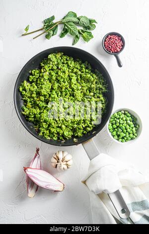 Mushy Erbsen Rezept gekochte Pfanne und Erbsen in Schüssel mit Minze Schalotte Pfeffer und Salz über weißen Stein Oberfläche Draufsicht Bio-Keto Lebensmittel lat flay ov Stockfoto