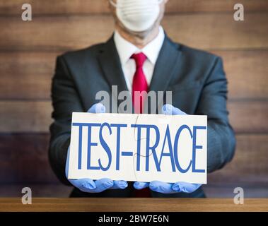 Ein Arzt, Geschäftsmann oder Arbeitgeber, der persönliche Schutzausrüstung trägt, Gesichtsmaske und blaue Handschuhe und ein Schild, das die Öffentlichkeit zum Testen und Trace auffordert Stockfoto