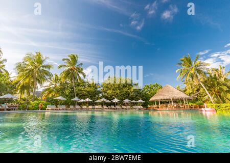 Sommer Outdoor-Tourismus-Landschaft. Luxuriöses Strandresort mit Swimmingpool und Liegestühlen oder Liegen unter Sonnenschirmen mit Palmen und blauem Himmel Stockfoto