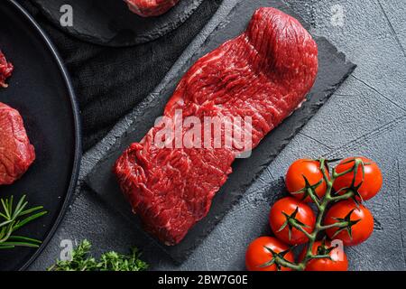 Rohes Tri-Tip-Cut schwarzes angus Bio-Steak auf schwarzem Teller und Steinschiefer mit Gewürzen, Kräutern grauen Beton Hintergrund. Nahaufnahme von oben Stockfoto