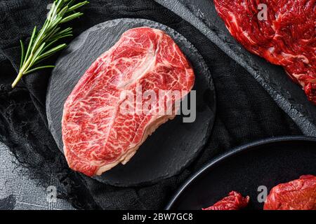 Rohe Spitze Klinge geschnitten schwarz angus Bio-Steak auf einem schwarzen Teller und Stein Schiefer mit Gewürzen, Kräuter grau Beton Hintergrund. Nahaufnahme von oben Stockfoto