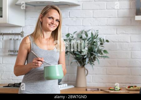 Porträt von fröhlichen Frau Kochen in der Küche zu Hause. Blonde lächelnde kaukasische Mädchen, die Kamera. Copyspace. Stockfoto