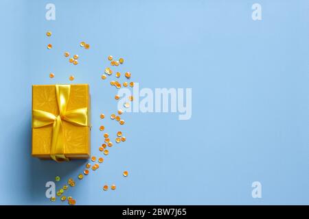 Gelbe Geschenkbox mit Party Konfetti auf blauem Hintergrund. Flaches Lay Stockfoto