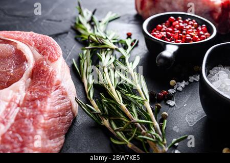 Rosmarin Kräuter Nahaufnahme auf schwarzen Stein Tisch mit Gewürzen und rohem Fleisch in der Nähe Ansicht selektive Fokus. Stockfoto