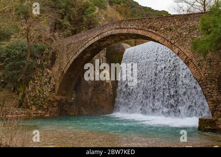 Eine alte Fußgängerzone aus Stein mit einem Wasserfall dahinter. Der Fluss überquert eine Schlucht, in Palaiokaria Trikala Griechenland. Es ist ein Wintermorgen. Stockfoto