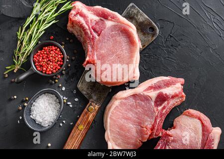 Rohe Schweinefleisch-Kotelett mit Kräutern und Gewürzen mit Fleisch american Cleaver auf schwarzem Hintergrund Raum für Text. Hochwertige Fotos Stockfoto