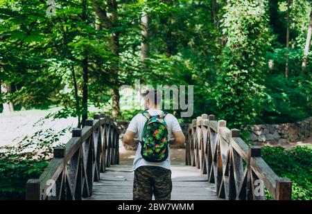 Sofia Park, Uman. Schöner Mann mit Rucksack auf einer Holzbrücke. Männlicher Wanderer auf einer Brücke zwischen grünen Sommerpark. Spaziergang im Sommer grün f Stockfoto