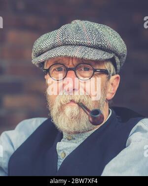 Vorderansicht, Porträt Nahaufnahme von isolierten, älteren 1940er Mann in flacher Kappe, rauchen eine Pfeife, im Freien bei 1940er WWII Sommerveranstaltung, Großbritannien. Stockfoto