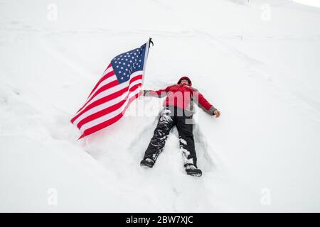 Ein Mann mit US-Flagge liegt im Schnee Stockfoto