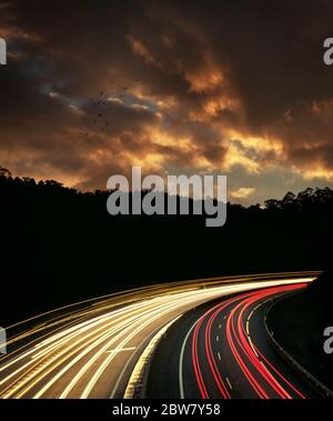 Kurve auf einer Straße mit leichten Wegen der vorbeifahrenden Autos Stockfoto