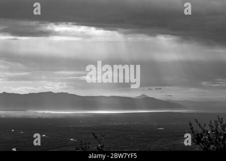 Sonnenstrahlen machen ihren Weg durch schwere Wolken über dem Meer in Nordgriechenland. Blick aus dem Hochwinkel von den Bergen in der griechischen Region Xanthi. Reisefoto in Schwarz und Weiß Stockfoto