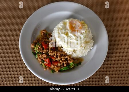 Thai Food, Reis gekrönt Rührei Huhn und Basilikum mit gebratenem Ei auf weißem Teller. Ist beliebtes Menü von Thailand Street Food, die eine starke würzige Fla hat Stockfoto