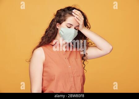 Kranke junge Frau mit Kopfschmerzen in Schutzmaske, die ihren Kopf berühren, während sie sich unwohl fühlt - sie hat kovid19 oder Kälte Stockfoto