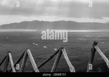 Holzzaun hoch in Bergen mit verschwommenen Sonnenstrahlen durch schwere Wolken über dem Meer in Nordgriechenland. Blick aus dem Hochwinkel von den Bergen in der griechischen Region Xanthi. Reisefoto in Schwarz und Weiß Stockfoto