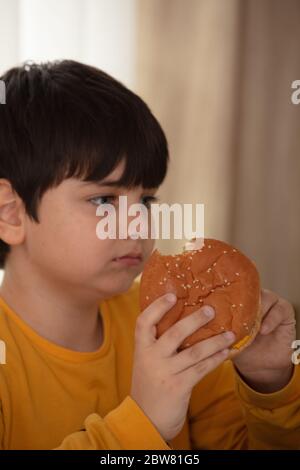 Nette gesunde Vorschule Kind Junge isst Hamburger sitzen in der Schule oder Kindergarten Café. Stockfoto