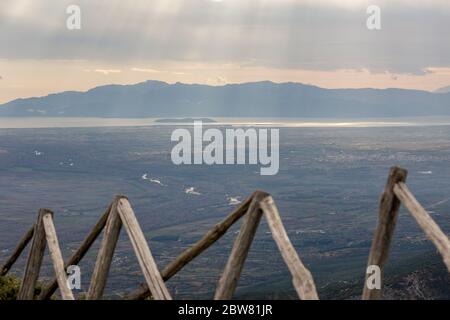 Sonnenstrahlen dringen in schwere Wolken über das Meer in Nordgriechenland ein. Blick aus dem Hochwinkel von den Bergen in der griechischen Region Xanthi. Schwarz-weiß Reisefoto, verwackelte Holzzäunung im Vordergrund Stockfoto