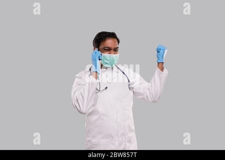 Arzt spricht am Telefon aufgeregt, trägt medizinische Maske und Handschuhe. Indischer Mann Arzt mit Telefon isoliert Stockfoto