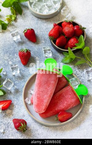 Selbstgemachter Erdbeer-Fruchtsaft. Eis oder Eiszapfen auf einem hellen Stein- oder Schiefertisch. Stockfoto