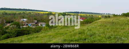 Ein kleines Dorf im Tal, dicke Bäume und Häuser zwischen den Feldern. Stockfoto