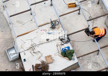 Ein Bauarbeiter schweißen eine quadratische Struktur aus Metallprofil, im Freien aus einem hohen Winkel Stockfoto