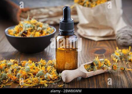 Tropfflasche Flasche mit ätherischem Öl, Infusion oder Serum, gesunde Ringelblumen in Schale und Papiertüte mit trockener Ringelblume auf Hintergrund. Herbal Me Stockfoto