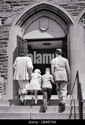 1940S 1950ER ZURÜCK ANSICHT DER FAMILIE VON VIER SCHRITTE NACH OBEN ZU KIRCHE EINGANG HALTEN HÄNDE - C62 HAR001 HARS STEIN VORSTADT STÄDTISCHEN STUFEN TÜR MÜTTER ALTE ZEIT NOSTALGIE BRUDER ALTE MODE SCHWESTER JUGENDLICH STIL KOMMUNIKATION SÖHNE FREUDE LEBENSSTIL RELIGION FEIER FRAUEN OSTERN VERHEIRATET SONNTAG BRÜDER LÄNDLICHEN EHEPARTNER EHEMÄNNER KOPIE RAUM IN VOLLER LÄNGE DAMEN TÖCHTER PERSONEN INSPIRATION MÄNNER CHRISTIAN GESCHWISTER SPIRITUALITÄT SCHWESTERN VÄTER B&W PARTNER ARCH RELIGIOUS CHRISTIANITY VÄTER LOW ANGLE DIRECTION HEAR VIEW UP GESCHWISTERVERBINDUNG KONZEPTIONELL VON HINTEN STILVOLLE UNTERSTÜTZUNG TREU Stockfoto