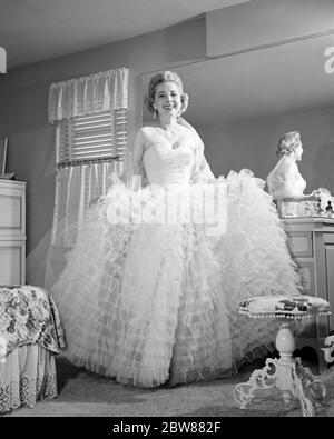 1950S 1960S LÄCHELNDE FRAU BLICK AUF KAMERA DURCH SCHLAFZIMMER SPIEGEL IN FORMELLE KLEIDUNG GEKLEIDET GEKRÄUSELT ABENDKLEID - F5433 DEB001 HARS HOME LIFE KOPIE RAUM IN VOLLER LÄNGE DAMEN PERSONEN B & W AUGE KONTAKT GLÜCK STILE AUFREGUNG NIEDRIGEN WINKEL ANLASS STOLZ LÄCHELT TRÄGERLOSEN FREUDIGEN RÜSCHEN STILVOLLE KLEIDUNG DEB001 MODE MITTE ERWACHSENE MITTE ERWACHSENE FRAU GEKRÄUSELT SCHWARZ-WEISS KAUKASISCHE ETHNIZITÄT IM VORDERGRUND ALTMODISCH Stockfoto