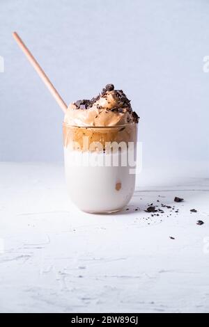 Dalgona Kaffee im Glas mit Schokoladenstückchen und Bambusstroh auf weißem Hintergrund. Vertikales Bild. Stockfoto