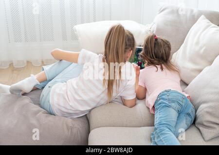 Zwei Schwestern liegen auf der Couch und verwenden Tablet, Draufsicht Stockfoto