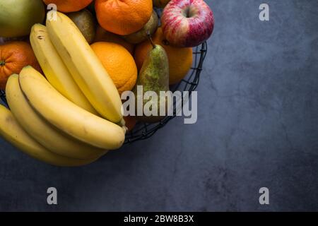 Äpfel, Bananen, Birnen, Mandarinen und Orangen auf einer Obstschale auf Betongrund. Gesunde Ernährung. Draufsicht. Kopierbereich. Stockfoto