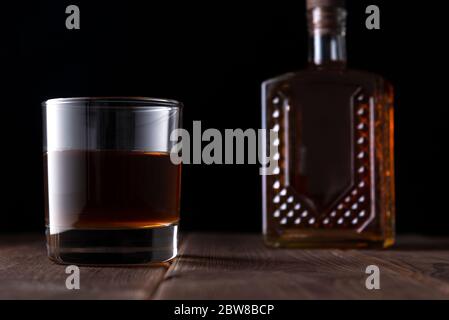 Flasche und Glas mit Alkohol auf einem Holztisch auf dunklem Hintergrund Stockfoto