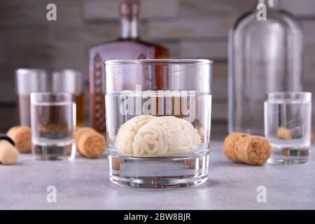 Menschliches Gehirn in einem Glas mit einem alkoholischen Getränk, vor dem Hintergrund von Flaschen mit Alkohol. Alkoholsucht. Schaden für das Gehirn durch Alkohol Stockfoto