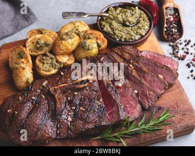 In Scheiben geschnitten saftiges gegrilltes Steak Medium seltenes Rindfleisch auf dem Knochen mit gerösteten neuen Kartoffeln Sauce Pesto Stockfoto