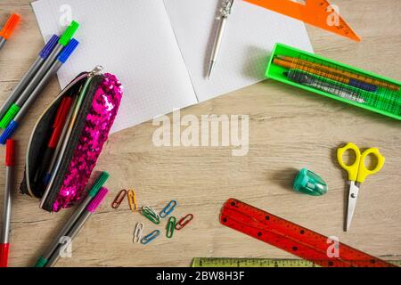 Schulbedarf liegt auf einem Holztisch. Briefpapier ist um den Tisch verstreut. Stockfoto