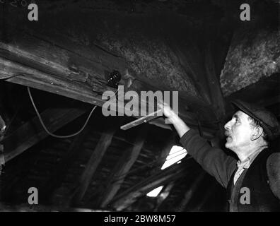 Ein Bauer weist auf einen elektrischen Schalter an den Balken in der alten Schmiede hin. 1935 . Stockfoto