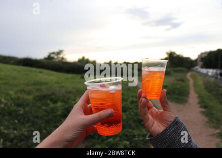 Zwei Hände halten aperol Spritz Cocktails in Plastikbechern Stockfoto