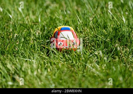 Kleine Kinder rot Kunststoff lächelndes Auto im Gras an einem sonnigen Tag versteckt. Stockfoto
