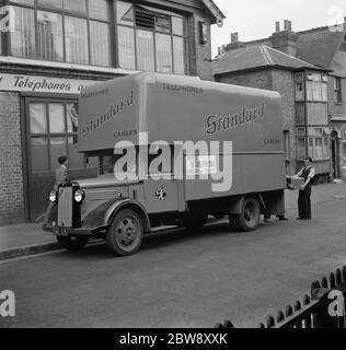 Ein Arbeiter lädt Kisten in einen Bedford LKW der Standard Telephone and Cables Company Ltd, vor ihrem Geschäft geparkt gehören. 1936 . Stockfoto