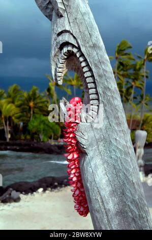 Wunderschöne rosa Plumeria lei hängt von der offenen Mündung eines hawaiianischen Tiki im Puuhonua o Honaunau National Historical Park auf der Big Island von Hawaii. Stockfoto