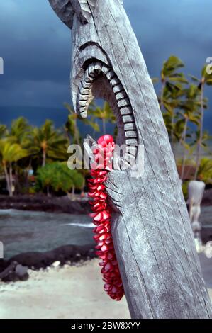 Wunderschöne rosa Plumeria lei hängt von der offenen Mündung eines hawaiianischen Tiki im Puuhonua o Honaunau National Historical Park auf der Big Island von Hawaii. Stockfoto